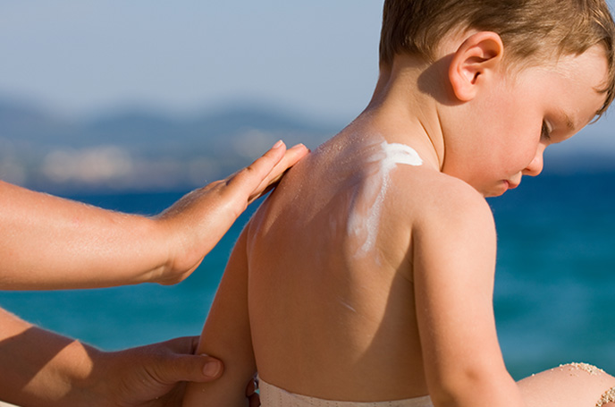Aplican crema solar en la espalda de un niño mientras está en la playa