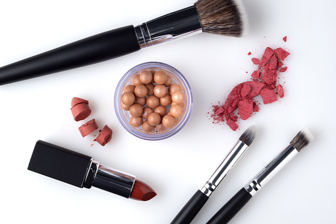 Productos de maquillaje con polímeros esparcidos sobre una mesa. Hay polvos de maquillaje, brochas, pintalabios y sombras de ojos.