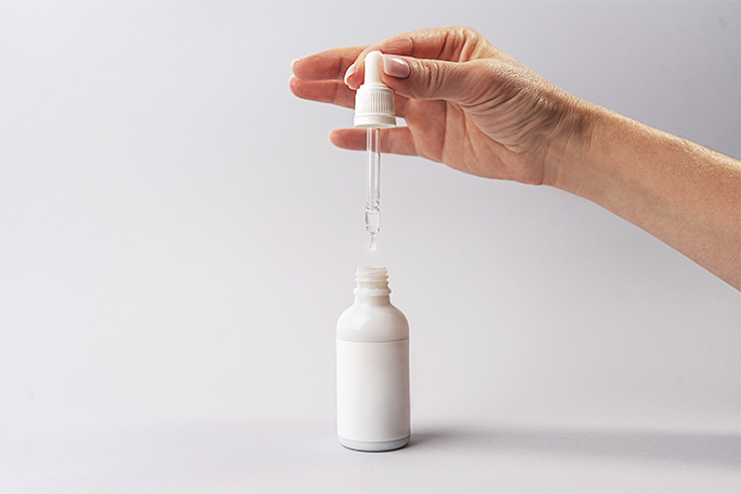 Mano de mujer cogiendo una pipeta de un sérum antiedad con retinol de una botella blanca