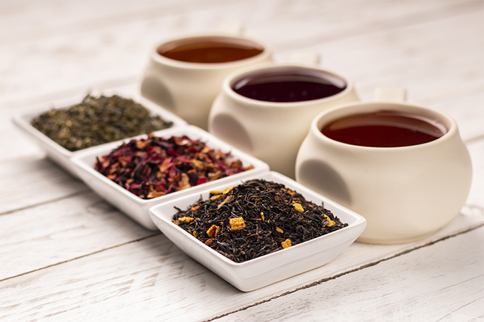 Tres variedades de té. Las hojas de té están en platos blancos y la infusión en tazas de porcelana.